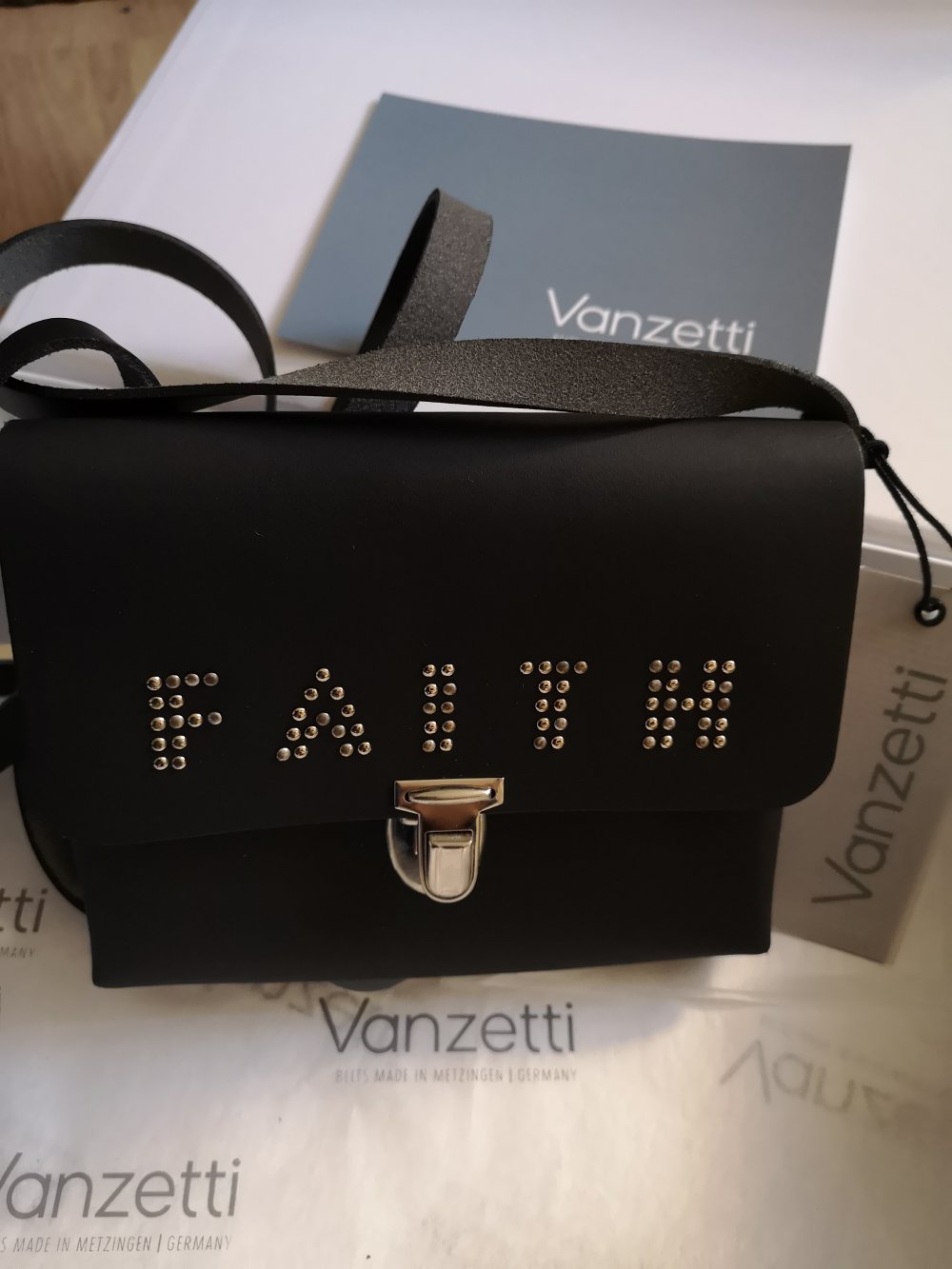 schwarze Schultertasche mit der Aufschrift Faith
