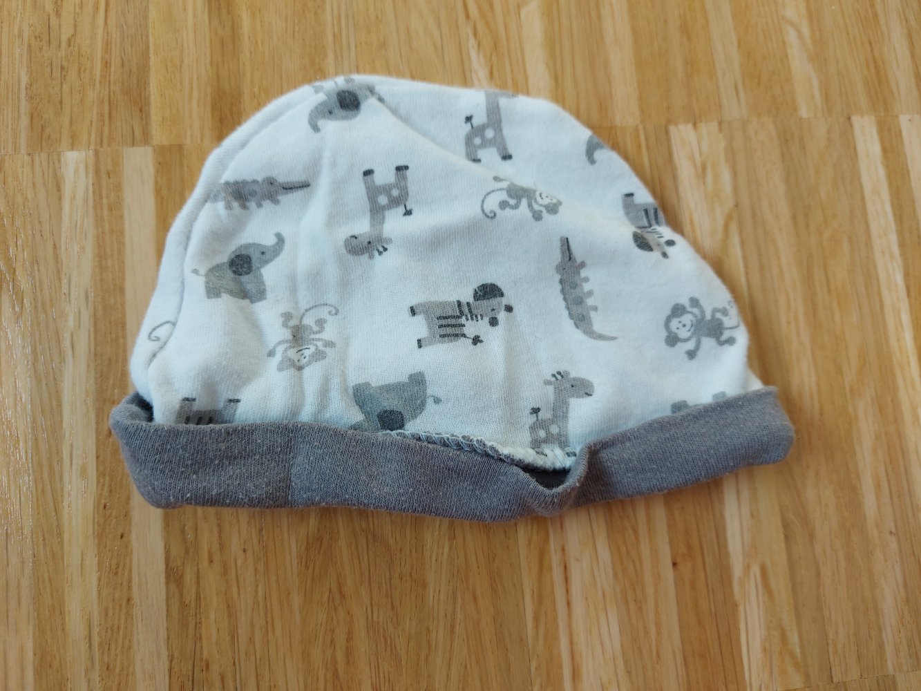 weiße Babymütze mit grauen Tiermotiven (Giraffe, Elefant, Affe usw.)