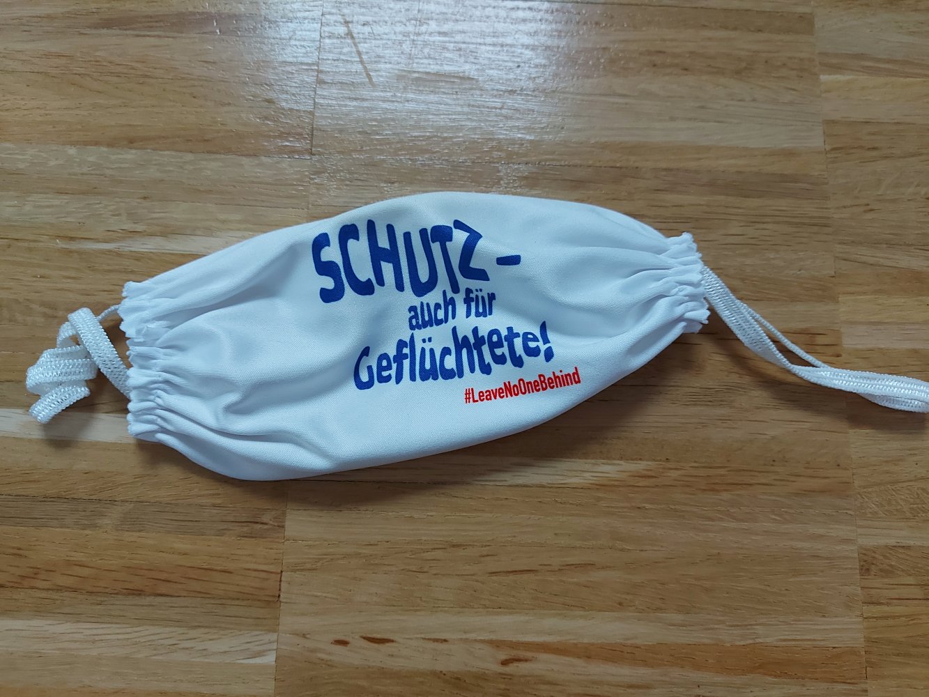 weiße Mund-Nasen-Bedeckung mit Statement Schutz- auch für Geflüchtete #LeaveNoOneBehind